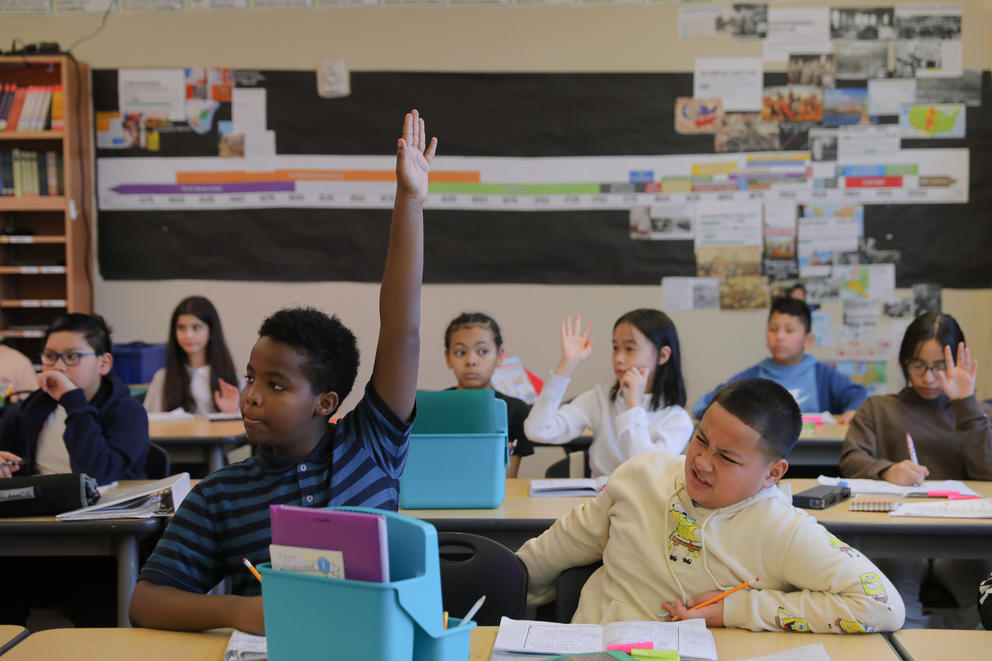 students raise their hands at their desks