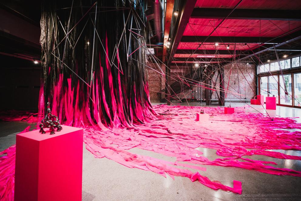 photo of a large open gallery with a giant hot pink and black fabric installation spilling through the space