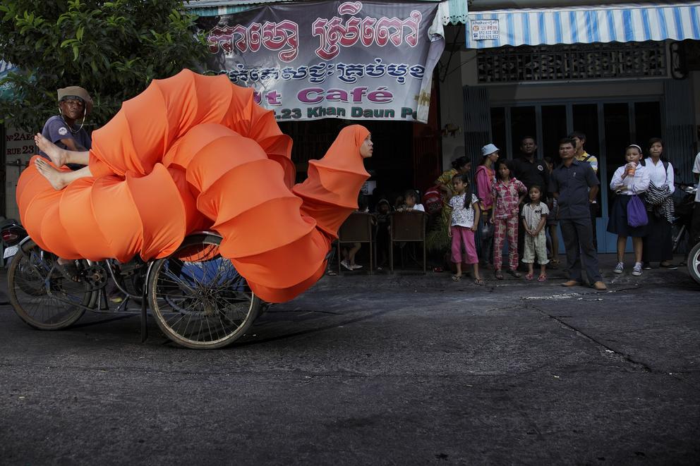photo of a busy cambodian street with an woman in an orange tube riding a bike