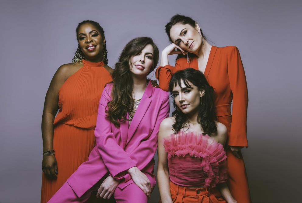 photo of four women standing close together, all wearing shades of pink and red