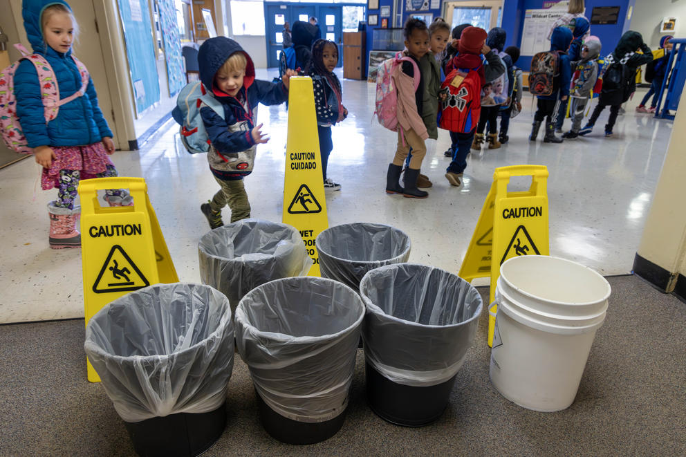 Children file past buckets with caution signs around them.