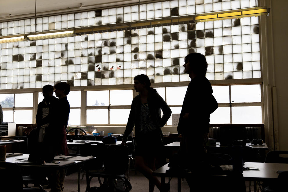 Students stand in front of a window that has panes that are broken or dirty.