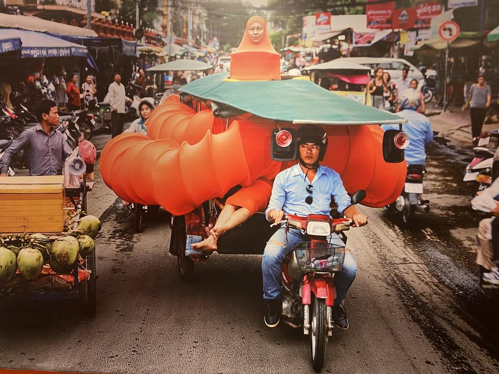 photo of an installation photo of a woman in an orange caterpillar costume on a moped cart
