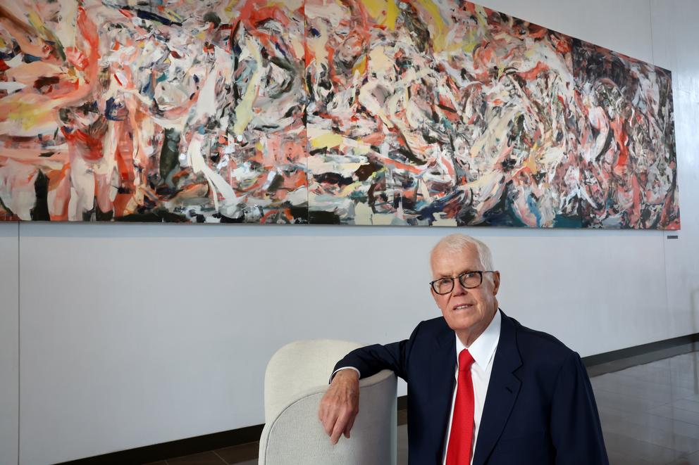 photo of a man in a suit sitting in front of a long horizontal abstract painting