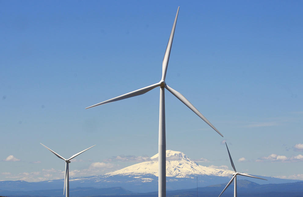 The propellors of a wind turbine are seen with a mountain in the background