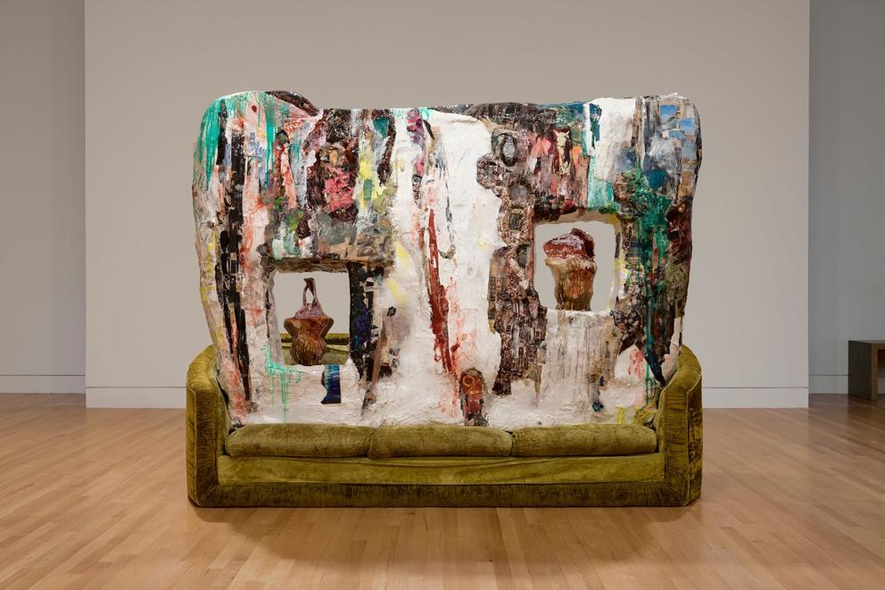 a large sculptural installation featuring a huge block of colored glazed clay sitting on an olive green sofa