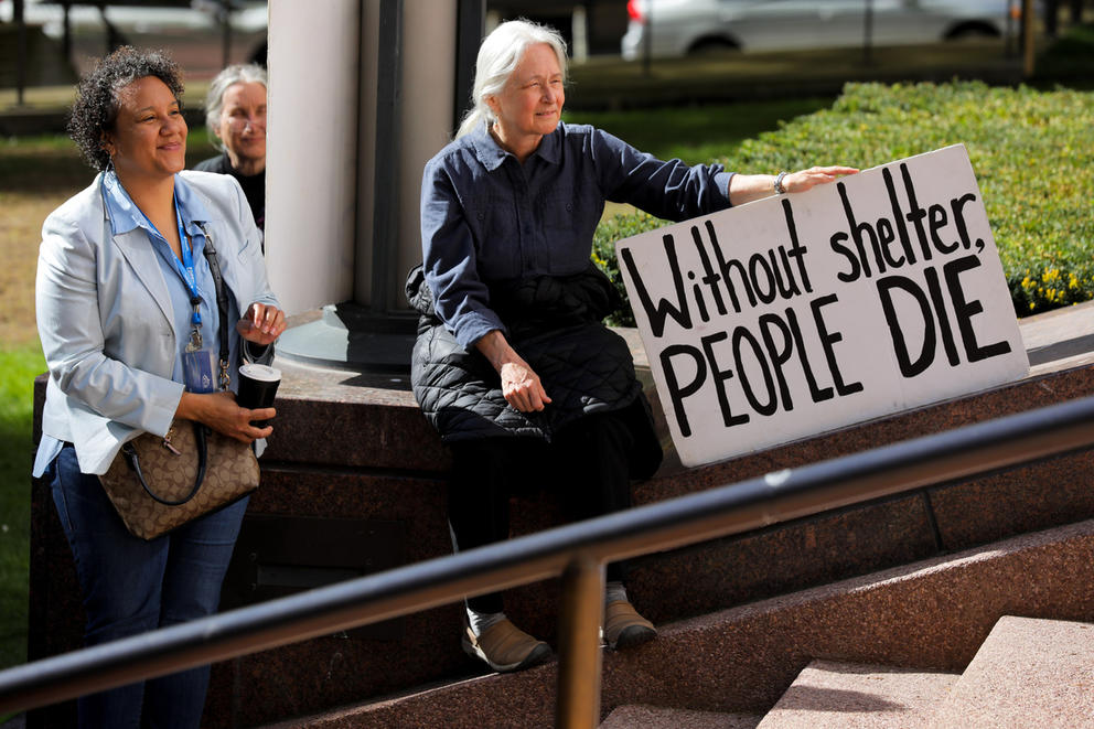 a woman sits on a ledge holding a sign that says without shelter people die
