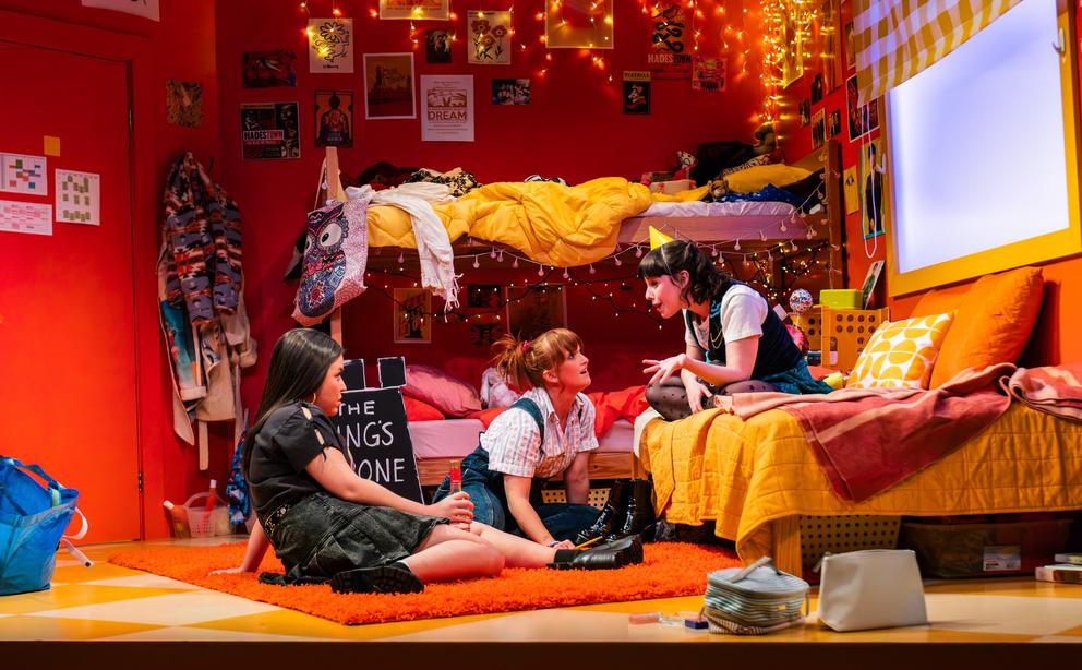 a play set in a highly decorated dorm room where three young women are talking