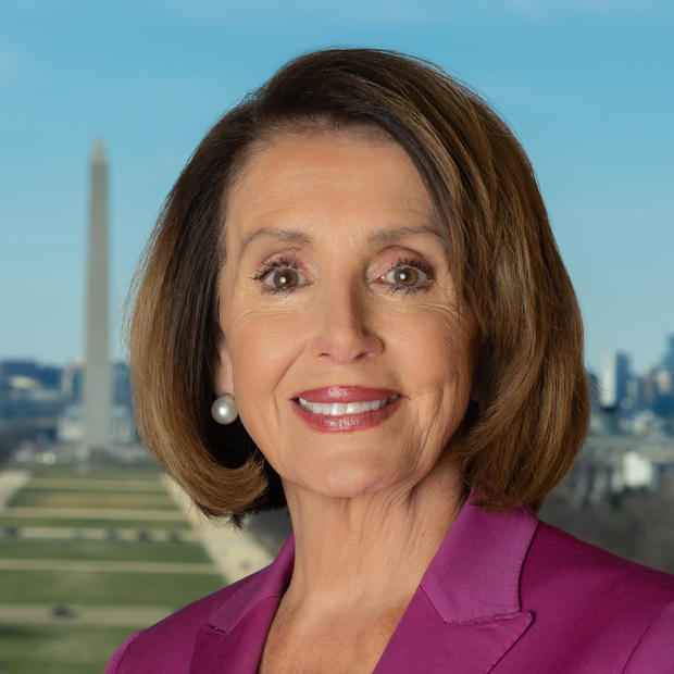 Older white woman with short, brown hear in a bob style cut wearing silver earrings, a white shirt and dark pink blazer against the backdrop of the National Mall in Washington, DC. The Washington memorial is visible. 