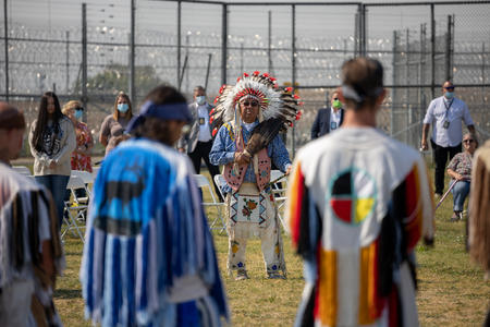 People in regalia stand listening to a speaker
