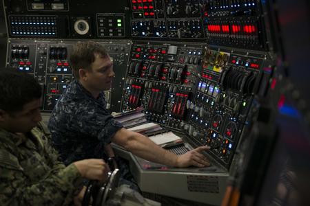 A sailor flips a switch on a large control panel for a submarine.