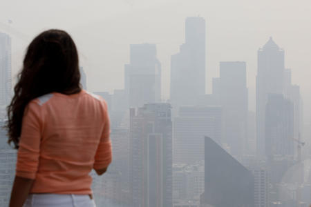 A woman looks at the skyline from the Space Needle observation deck on Monday, Aug. 20, 2018 in Seattle. Haze from wildfires caused a decrease in air quality in the area. (Photo by Sarah Hoffman/Crosscut)