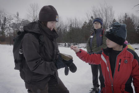 A woman shows a young boy a rock while standing in the snow