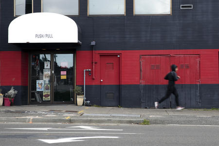 A person running past a red and gray shop front. 