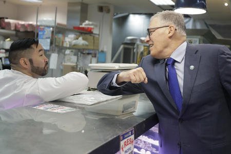 Washington Gov. Jay Inslee, right, bumps elbows with a worker at the seafood counter of the Uwajimaya Asian Food and Gift Market