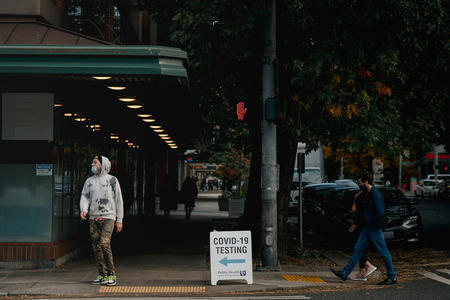 People wearing masks walk by a sign offering COVID-19 testing.