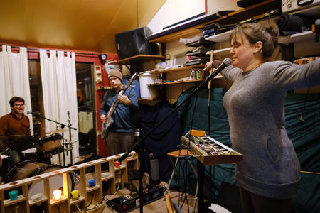 A drummer, guitarist and singer in a small rehearsal space.