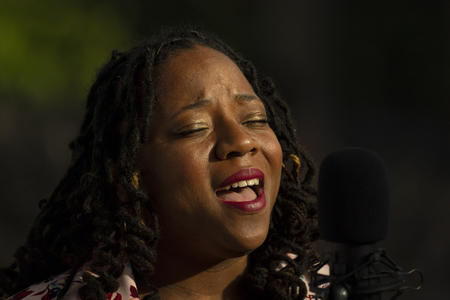 Person with eyes closed, sunlight on her face, mouth open because she is singing ("Lift every voice and sing," the Black national anthem)