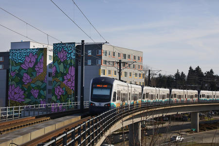 a light rail train passes by an apartment building in Seattle