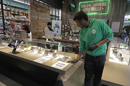 Man in green hoodie wipes a display case, with sign and other customers in background