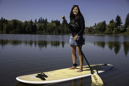 smiling woman standing on paddle board in a lake lined with trees