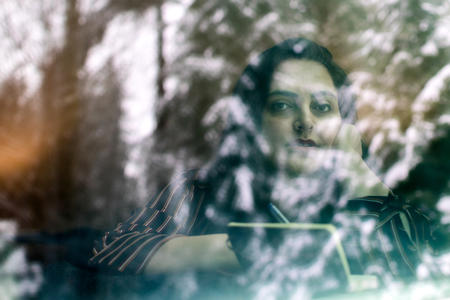 A woman looks through a window with her face partially obscured by a reflection