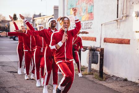 six people in a line, all wearing red tracksuits and dancing