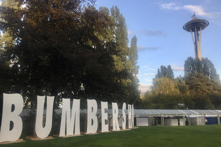 Seattle Center grounds with Space Needle in the distance and large cardboard letters spelling out BUMBERSHOOT