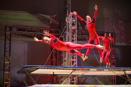 three acrobats in red unitards leap on a trampoline