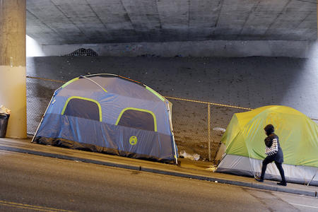 A person walks up a hill next to tents lined up beneath a highway adjacent to downtown Seattle, Wednesday, March 8, 2017. (AP Photo/Elaine Thompson)