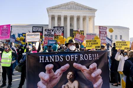 Protesters outside the U.S. Supreme Court hold signs, including one in the foreground that says "Hands Off Roe" with an image of hands lunging forward