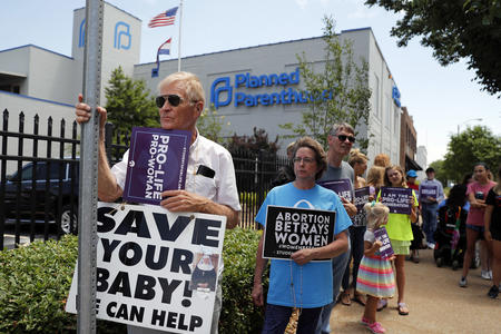 A line of protesters hold signs reading "Pro-life Pro-woman," "Abortion betrays women," and "Save your baby! We can help"