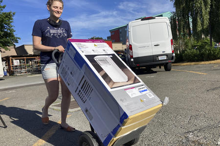 a smiling person wheels a cart holding an air conditioning unit