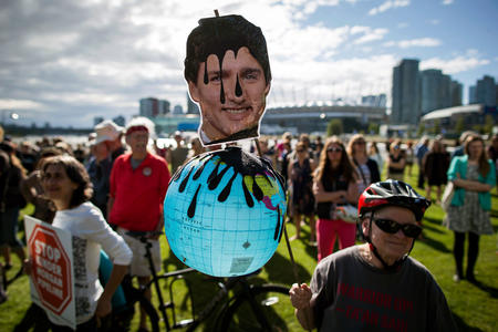 A protester holds a photo of Canadian Prime Minister Justin Trudeau and a representation of the globe during a protest against the Kinder Morgan's Trans Mountain pipeline expansion, in Vancouver, British Columbia, Tuesday, May 29, 2018. Canada's federal government said Tuesday it is buying the controversial pipeline from the Alberta oil sands to the Pacific Coast to ensure it gets built. (Darryl Dyck/The Canadian Press via AP)