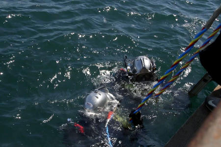 Two divers wearing metal helmets descend into the ocean