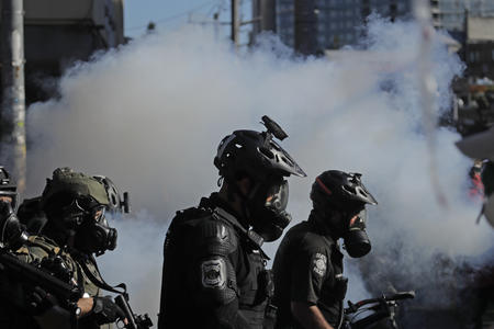 Police officers silhouetted in front of cloud of tear gas