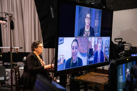 A monitor in a studio shows three interview guests