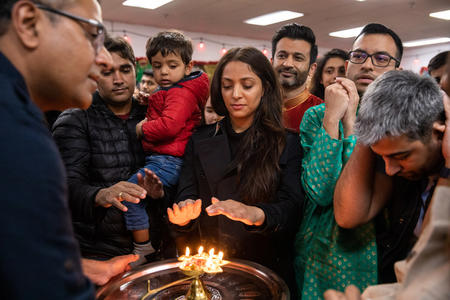 People gather around a plate with candles, a woman holds her hands over the flame