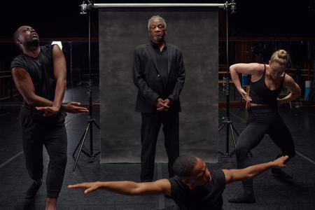 a man in front of a gray backdrop with dancers posed around him