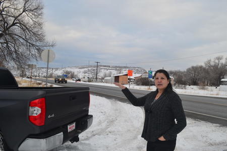 A woman stands next to her truck along a snowy road with her hand outstretched
