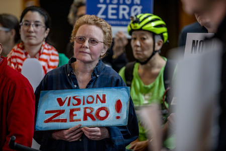Woman protestor in crowd holding sign reading vision zero 