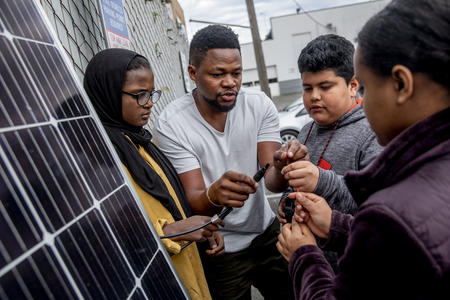 Edwin Ngugi Wanji, center, teaches a group of kids from the Lake City Young Leaders program about how to work a solar panel at the Lake City Community Center on April 1.