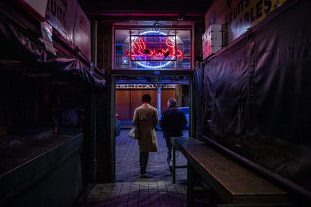 two people walk through doorway under neon sign