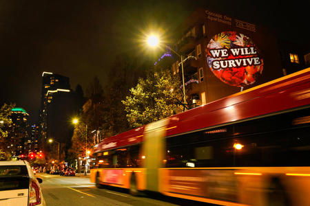 A bus passes by a building with a projected image of a balloon with "We Will Survive" on its side
