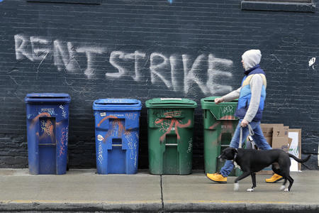man walking a dog in front of "rent strike" grafitti
