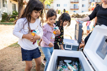 Three children pick up food from a cooler.
