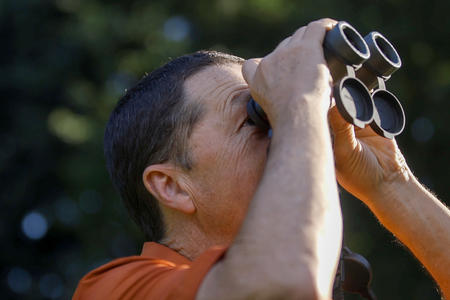 Stephen with binoculars to his face looking up