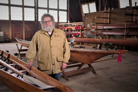 Knute Berger stands between a Husky shell and Native canoe at inside the UW Shellhouse