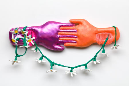 Two hands holding each other connected by a green garland. Hand on left is purple and hand on right is orange.