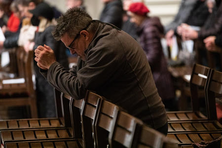a man kneels in prayer over a pew
